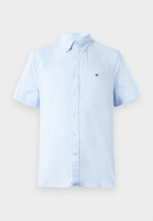 Šviesiai mėlynas trumpomis rankovėmis mygtukinis marškinėliai, pagaminti iš medvilnės. Turi klasikinį apykaklę ir nedidelį logotipą ant krūtinės. Lygus paviršius.