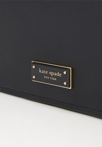 Navy blue purse made of smooth leather featuring a gold-tone plaque with "kate spade NEW YORK" text and decorative studs.