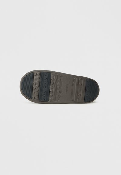 Suela de zapato de goma con un patrón de círculos elevados y surcos. Predominantemente gris con un acento texturizado negro en el talón.