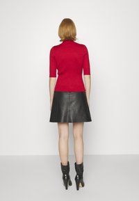 Röd ribbad kortärmad topp matchad med en svart läderkjol med utsvängd nederkant. Modellen bär svarta klackade ankelskor. Släta texturer och djärva färger.