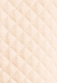 Beiger, gestepptes Gewebe mit einem Rautenmuster, das eine weiche Textur und gleichmäßige Nähte über die gesamte Oberfläche zeigt.