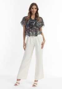 Gennemsigtig sort-hvid bluse med slangeprint-design, flæseærmer og peplum talje, parret med cremegule brede bukser og hvide hæle.