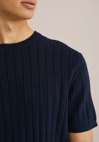 Tamsiai mėlyna megzta trumpų rankovių marškinėliai su vertikaliu raukšlėtu raštu ir apvalia apykakle. Minkšta medžiaga, turinti prigludusią siluetą.