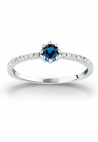 Silverring med en central blå safir omgiven av små klara stenar längs bandet, med en delikat, polerad yta.