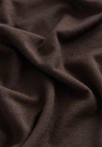 Weicher, dunkelbrauner Strickstoff mit sichtbarer Rippenstruktur und natürlichen Falten, die Schatten und Highlights erzeugen.