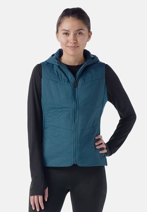 Türkisfarbene isolierte Weste mit Kapuze, ausgestattet mit einem Reißverschluss und vertikaler Steppung auf der Brust. Schwarzes Langarmshirt darunter.