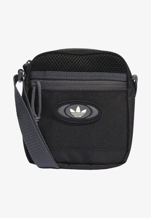 Petit sac bandoulière noir compact avec bandoulière réglable grise, poche avant zippée, panneau supérieur en mesh et logo ovale avec emblème de feuille stylisée.