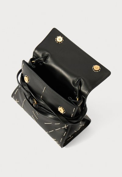 Black leather handbag with contrasting white stitching and gold hardware. Open top with a spacious interior and adjustable strap.