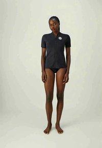 Rash guard black cu mâneci scurte, cu fermoar frontal și patch cu logo. Textură netedă și design ajustat, asociat cu pantaloni de baie închis la culoare.