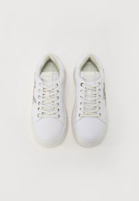 Sneakers bianchi in tela con punte rotonde, lacci, suola in gomma rigata e un accento metallico decorativo sul lato. Design minimalista e semplice.