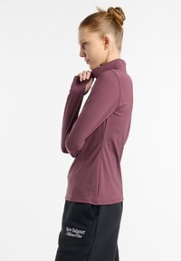 Langærmet, getailleerd top van mauve stof met een hoge kraag en duimgaten, gecombineerd met zwarte sweatpants met witte logo-details.