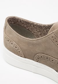 Chaussure en daim marron clair avec motifs décoratifs perforés, doublure en tissu floral et semelle épaisse en caoutchouc blanc, vue de côté et légèrement par-dessus.
