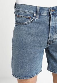 Shorts de mezclilla en azul claro con un acabado desgastado. Cuenta con cinco bolsillos, cierre de cremallera y botón de metal. Dobladillo sin terminar en las piernas.