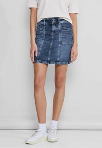 Denim minikjol i mörkblått, med en figursydd design, framfickor och knappstängning. Kjolens kant slutar vid mitten av låret. Matchas med vita sneakers.