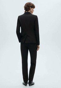 Svart skräddarsydd kostym med slim fit, med en enda vent bak, och matchande slim byxor. Slät tygkänsla, minimalistisk design.