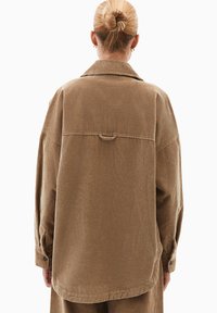 Giacca camicia in corduroy marrone con una vestibilità ampia, tessuto testurizzato e righe verticali prominenti; include un colletto e polsini con bottoni.