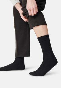 Svart bomullsblandning strumpor med ribbat manschett, matchade med mörka byxor, som framhäver strumpans textur och passform.