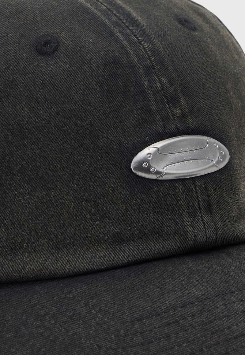 Casquette de baseball noire avec une petite broche argentée en forme de poisson stylisé, attachée près de la couture du panneau avant.