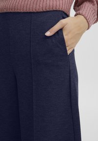 Marineblauwe wijde broek van een gestructureerde stof. Bevat zijzakken en heeft een gladde afwerking. Gepaard met een lichtroze gebreide trui.
