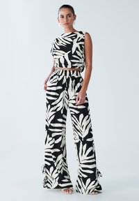 Melnbalts raksts divdaļīgais tērps, kas sastāv no īsa tops un plašām biksēm ar elastīgu jostu un saistītām detaļām apakšmalā.