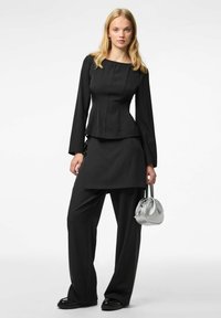 Completo nero elegante composto da un top aderente a maniche lunghe con scollatura quadrata e pantaloni a vita alta e gamba larga, abbinato a una borsa argentata.