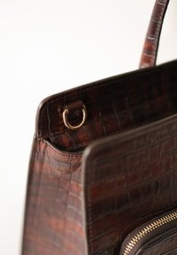 Brown crocodile-embossed leather handbag featuring a gold-tone hardware ring and a zippered pocket along the side.