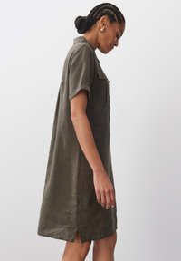 Olivengrünes Leinen-Shirtkleid mit kurzen Ärmeln, geknöpftem Brusttaschen und seitlichem Schlitz. Es hat eine lockere Passform und eine glatte Textur.