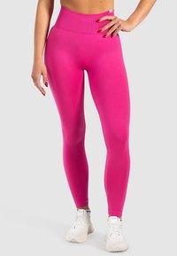 Korkeavyötäröiset, vartalonmyötäiset leggingsit kirkkaanpinkerissä kankaassa, jossa on teksturoitu vyötärönauha ja sileä pinta, yhdistettynä valkoisiin lenkkareihin.