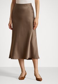 Brun sateng midi skjørt med en jevn tekstur, utsvingt design og en lett asymmetrisk kant. Brukt med brune blokkhæl sko.