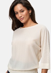 Pull en tricot couleur crème avec un motif ondulé, décolleté bateau et manches trois-quarts. Texture douce avec des poignets côtelés.
