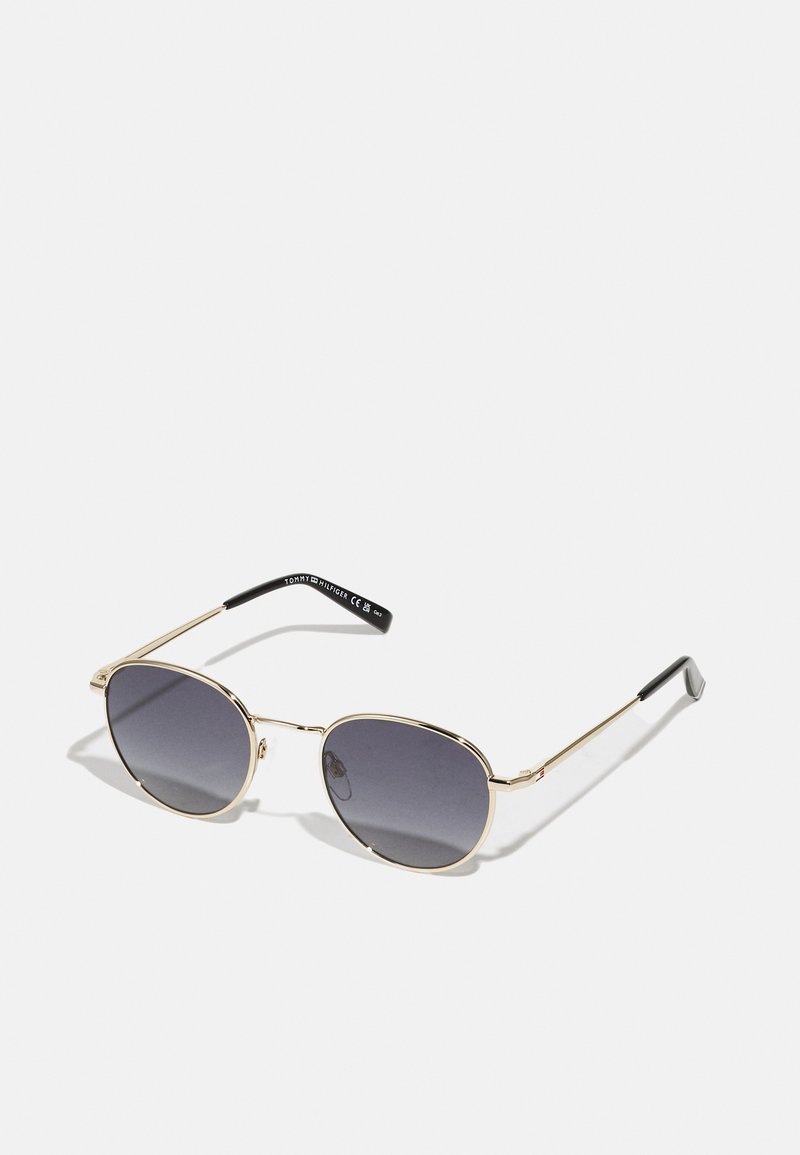 Gold metal sunglasses with rounded lenses, dark gradient tint, slim temples, and a black plastic tip on each arm.