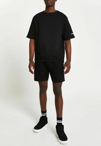 Black sweatshirt with short sleeves and crew neck paired with black shorts. Worn with black high-top sneakers and striped socks.