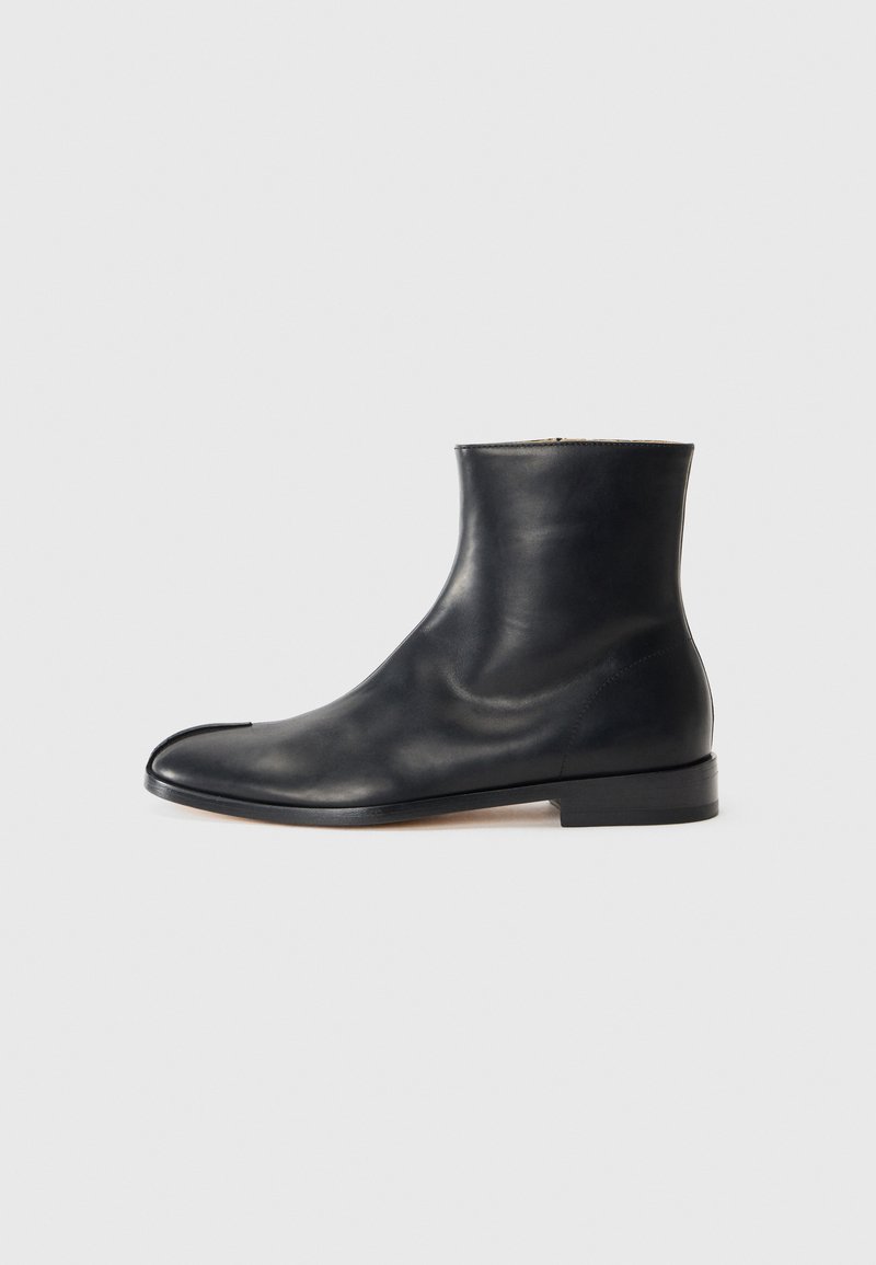 Stivale alla caviglia in pelle nera con finitura liscia, punta arrotondata, design minimalista e tacco piatto. Silhouette classica adatta a diverse occasioni.
