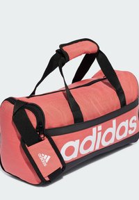 Borsa da viaggio corallo con accenti neri, chiusura con zip e manico regolabile. Presenta un grande logo Adidas bianco sul lato e un materiale resistente.