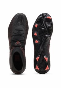 Μαύρα και κόκκινα ποδοσφαιρικά παπούτσια με υφασμένους επάνω μέρη και κωνικά καρφιά, με προβολή από πάνω και σόλα με πορτοκαλί τριγωνικά στοιχεία πρόσφυσης.