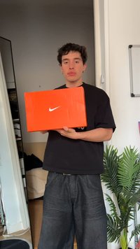 Oranž šuvikast, mida hoiab inimene, kus on nähtav suur valge swoosh logo. Taustal on taim ja toakujundus.