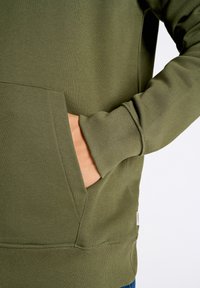 Sudadera verde oliva con una textura suave, que presenta un bolsillo canguro y puños redondeados. Los detalles en las costuras realzan el diseño.