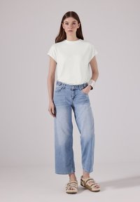Bílý krátký rukáv tričko, světle modré široké džíny a huňaté béžové pantofle s dvojitými popruhy. Jednoduchý, ležérní outfit.