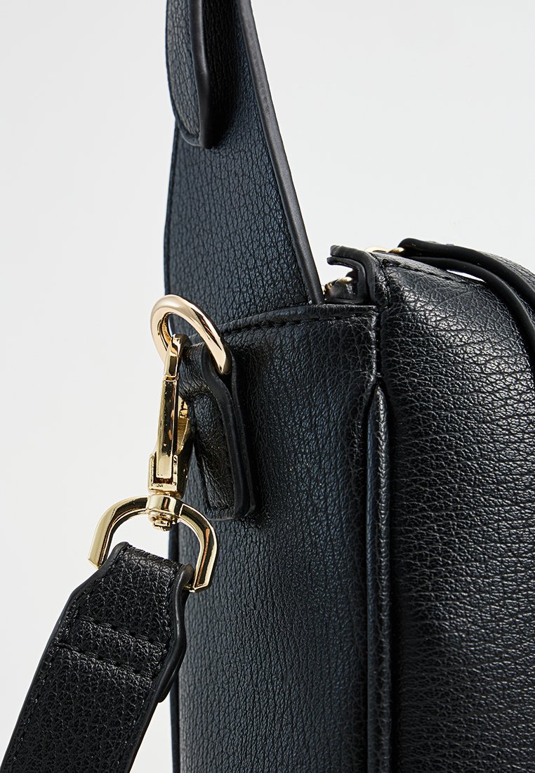 Sac en cuir noir texturé avec une fermeture à crochet en métal doré et une bandoulière réglable, mettant en avant des lignes épurées et un design structuré.