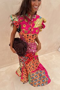 Kleurrijke jurk met een patroon en enerverende mouwen, in warme tinten van roze, oranje en rood. Vergezeld door een donkerbruine clutch.