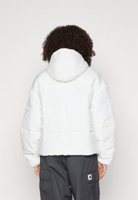 Vit quiltad pufferjacka med huva, med en boxig design och synlig söm. Tyget ser slätt och mjukt ut.