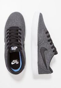 Svarta och grå tygsnickers med en texturerad finish, vit gummisula och svart Nike-logotypaccent. Klassisk snörningsdesign.