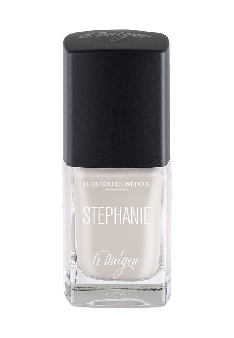 Nagellack in einer klaren Glasflasche mit quadratischem Boden, ausgestattet mit einem schwarzen, schrägen Deckel. Der Lack hat eine sanfte, neutrale Beigetönung.