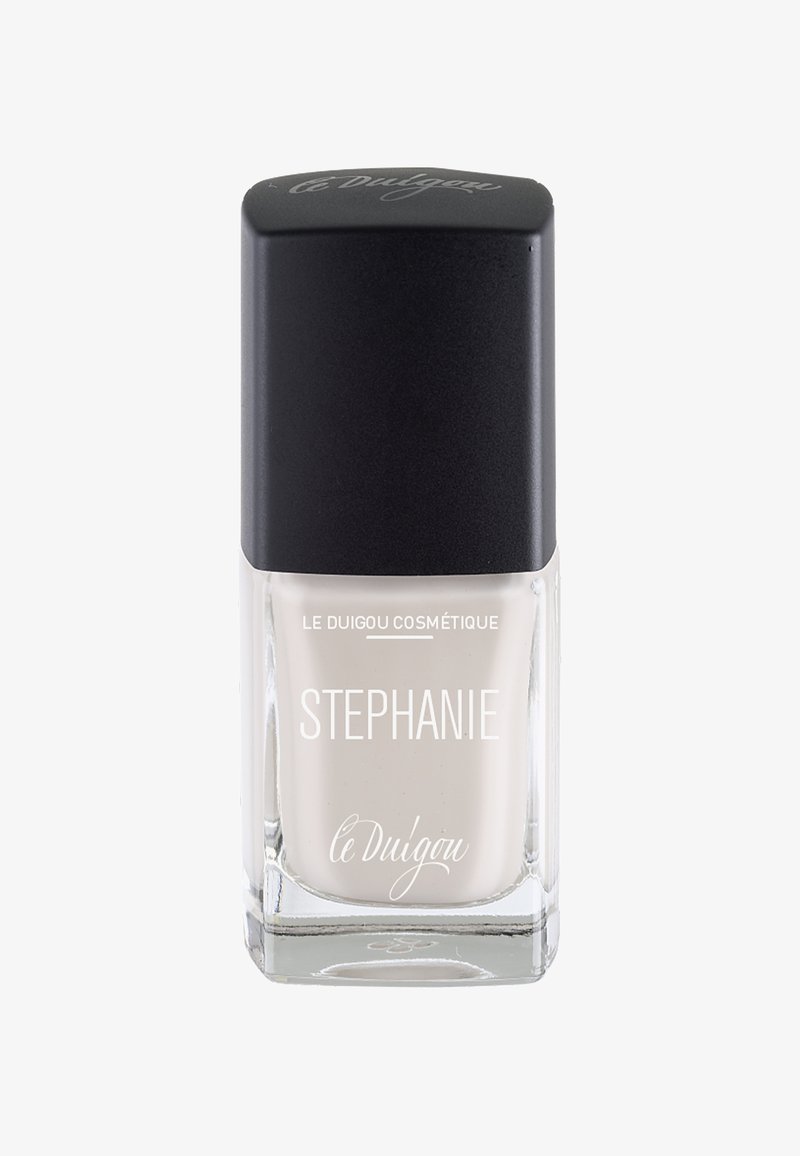 Nagellack in einer klaren Glasflasche mit quadratischem Boden, ausgestattet mit einem schwarzen, schrägen Deckel. Der Lack hat eine sanfte, neutrale Beigetönung.