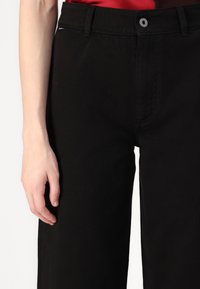 Pantalones de mezclilla negros con corte recto, con cierre frontal de botón, trabillas para cinturón y bolsillos laterales. Textura suave, diseño casual.