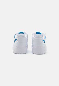 White sneakers with blue accents, smooth leather upper, padded collar, round toe, and a thick rubber sole, displaying a simple design.