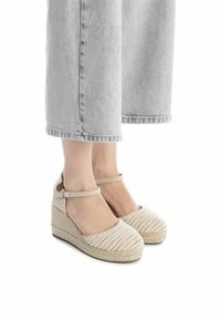 Sandales compensées avec une tige tressée beige, bout rond et bride de cheville ajustable. Talon compensé en jute texturé.