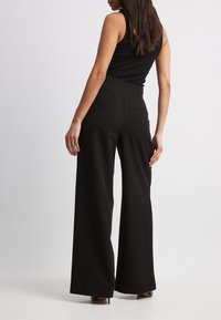 Zwarte wijde broek met een hoge tailleband. Zacht materiaal, twee achterzakken en een vloeiende silhouet, gecombineerd met zwarte hakken.