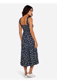 Marineblaues Kleid mit Blumenmuster, tailliertem Oberteil, Rüschenträgern und gestuftem Rock. Kombiniert mit weißen Sneakers für einen lässigen Look.