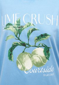 Πράσινες μπάλες τένις σε ένα φυλλώδες κλαδί με το κείμενο "LIME CRUSH" και "Courtside fruit club" σε φόντο από ανοιχτό γαλάζιο ύφασμα.